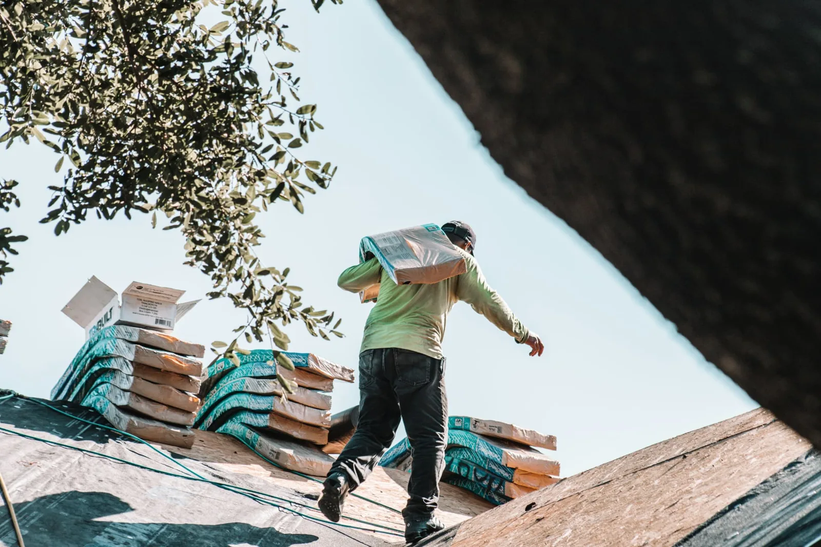 Roofer carrying shingle bundles across a rooftop
